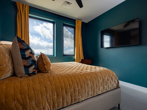 Unwind in this cozy bedroom with bold teal walls, a plush golden bed, and natural light streaming through your windows. Your peaceful retreat awaits, complete with modern amenities for total comfort.