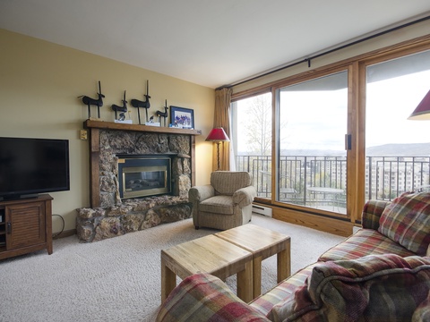 Unwind in your cozy living room with a stone fireplace, plush seating, and stunning mountain views through expansive windows—perfect for relaxing after a day of adventure.