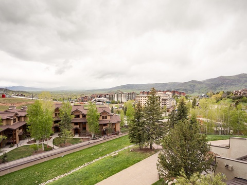 Mountain resort setting with residential chalets and green spring landscapes framing the valley below. The property sits amid a scenic alpine community.