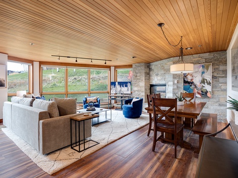 Unwind in this sun-drenched living space where rich wood tones meet modern comfort. Sink into plush seating, enjoy hillside views through expansive windows, and gather at the dining table beneath the warmth of natural wood ceilings.