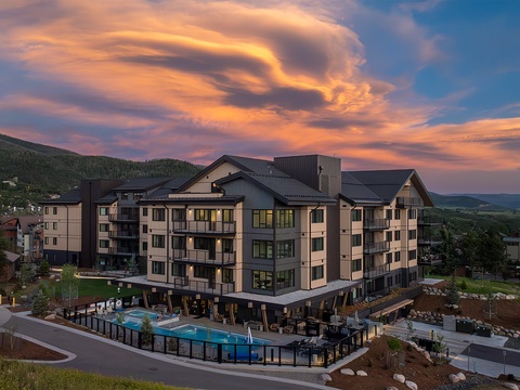 This mountain property welcomes guests with sweeping views of forested slopes and valley landscapes, set beneath dramatic alpine skies at day's end.