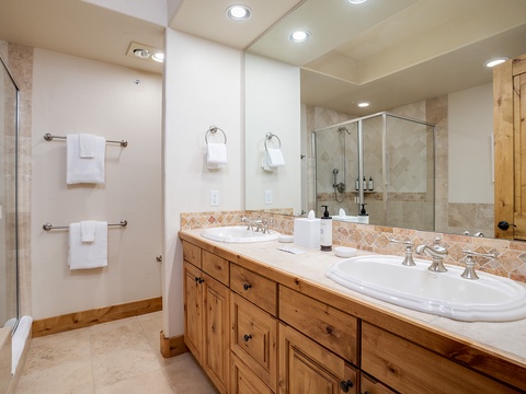 Step into your spacious dual-sink bathroom with a walk-in shower, warm wood cabinetry, fresh towels, and ample counter space for your comfort.