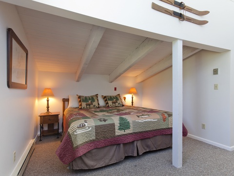 Cozy attic bedroom with vaulted wood-beam ceilings, warm bedside lamps, and rustic ski decor to make you feel right at home in the mountains.