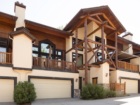 A stunning mountain property showcasing rustic timber-frame architecture, multi-level balconies, and private garages, blending natural wood tones with stucco finishes in a serene residential setting.