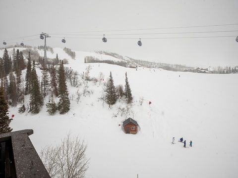 Ski slopes blanketed in fresh powder with a gondola lift ascending to snow-capped peaks, surrounded by evergreen forest and mountain structures, offering winter sports access.