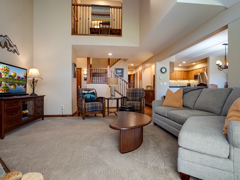 Settle into the airy living room with soaring ceilings, cozy seating, and a fully equipped kitchen just steps away—your perfect home base for mountain memories.