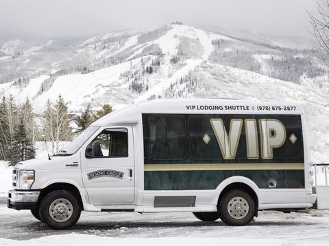 VIP shuttle ready to transport guests against a dramatic winter mountain backdrop covered in fresh snow and skiing terrain.