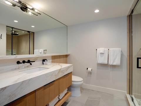 Step into your modern sanctuary featuring a sleek marble vanity, spacious walk-in shower, and crisp white linens—your personal retreat for unwinding after a day of exploring.