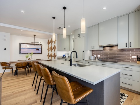You'll love gathering in this sleek, open kitchen with its spacious island, modern pendant lighting, and warm caramel leather seating—perfect for morning coffee or evening meals together.
