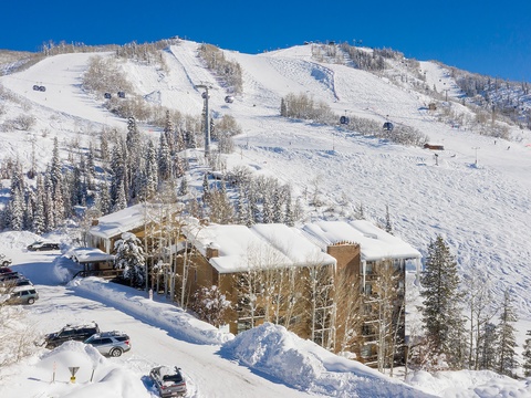 Aerial view of the property nestled at the base of ski slopes, with direct access to chairlifts and winter mountain terrain. The surrounding area offers pristine snow-covered peaks and ski runs.