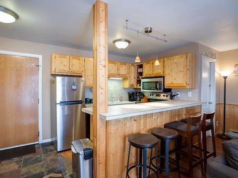 Gather around the welcoming kitchen island with seating for four, where stainless steel appliances and warm wood cabinetry create a relaxed mountain retreat vibe for your culinary adventures.