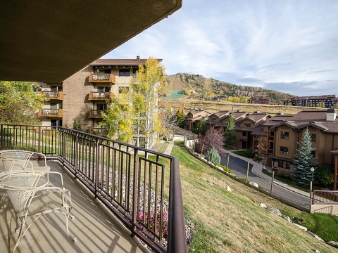A private balcony overlooks a peaceful mountain community framed by golden aspens, ski slopes, and neighboring vacation homes—perfect for morning coffee or evening relaxation surrounded by scenic beauty.