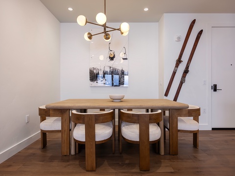 Your ski-chic dining area features a stunning wooden table with cozy seating for six, illuminated by modern lighting and accented with vintage skis—a perfect spot to share stories after a day on the slopes.