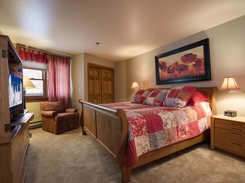 Settle into your cozy bedroom with warm wood furnishings, a plush quilted bed, and soft lighting that invites restful nights after mountain adventures.