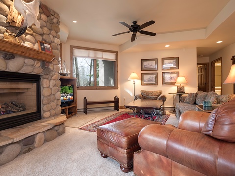Unwind in your spacious living room with a cozy stone fireplace, plush leather seating, and warm lighting perfect for evenings after exploring nearby trails.