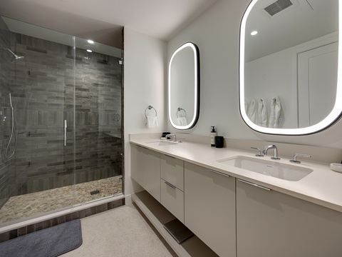 Step into your serene spa-like bathroom where a sleek walk-in shower with contemporary tiling awaits. Dual vanities with elegant backlit mirrors give you plenty of space to unwind and refresh.