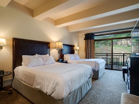 Sink into cloud-like comfort in your spacious room with two plush beds, elegant dark leather headboards, and a private balcony framing stunning mountain views.