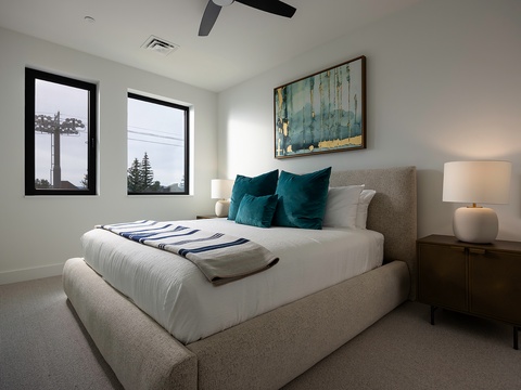 Unwind in your serene bedroom featuring a plush bed, soothing coastal art, and soft lighting. A ceiling fan keeps you comfortable, while natural light from the windows brightens your retreat.