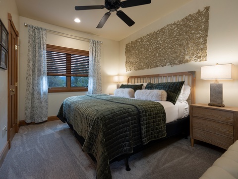 Sink into the plush bed under soft lighting, where textured wall art and a gentle ceiling fan create your perfect retreat after a day of adventure.