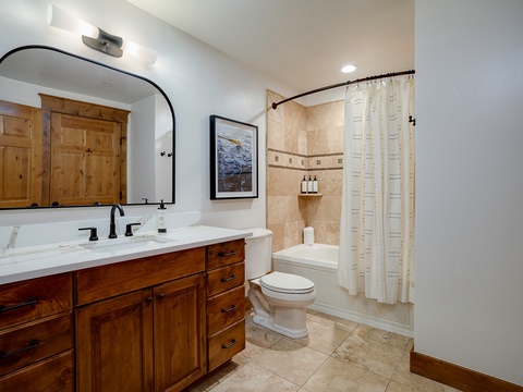 Your bathroom blends rustic charm with modern elegance, featuring warm wood cabinetry, polished marble countertops, and a tiled shower with toiletries ready for your arrival.