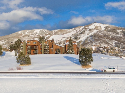 Modern mountain lodges nestled against pristine snow-covered peaks, perfectly positioned for winter adventures. The property sits in a scenic alpine valley with ski slopes visible in the distance.
