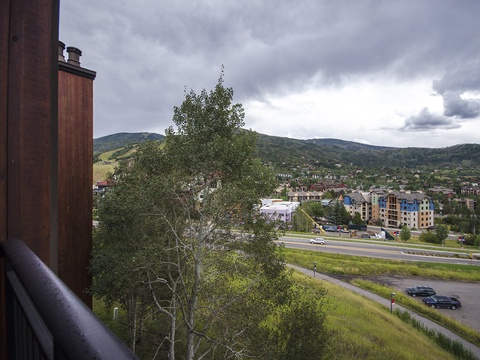 Panoramic view from your private balcony overlooking rolling mountains, verdant valleys, and the charming town below, with dramatic clouds painting the expansive sky.