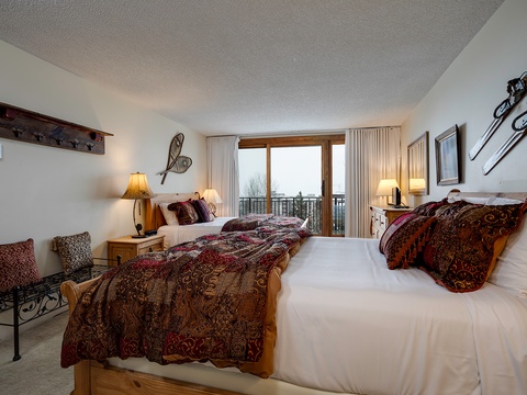 Settle into your spacious retreat with two comfortable beds dressed in rich textures, warm lighting, and a private balcony framing peaceful views beyond.
