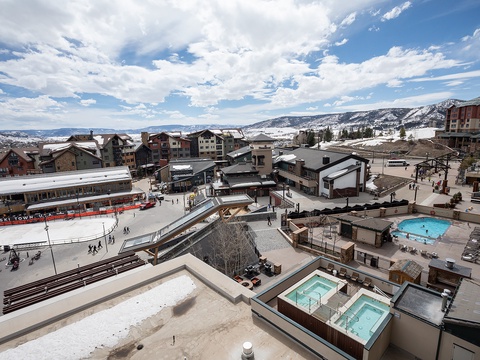 Elevated view of a mountain resort community featuring ski facilities, swimming pools, hot tubs, and snow-covered slopes, showcasing the property's winter recreation amenities and surrounding alpine landscape.
