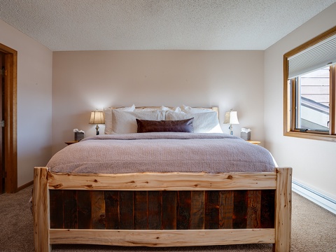 Sink into plush comfort after your mountain adventures in this serene bedroom, where rustic wood meets soft linens and warm lamplight creates your perfect retreat.