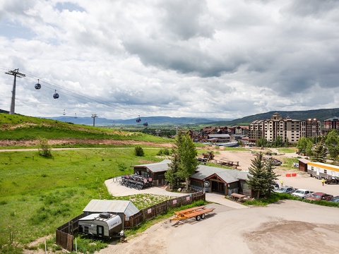 Aerial view of the property and surrounding mountain resort area, featuring gondola lifts, green slopes, and nearby lodging buildings.