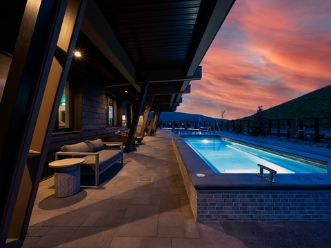 The property rests at the edge of a pristine mountain landscape, where vibrant sunsets paint the sky in dramatic shades of pink and orange above forested peaks.