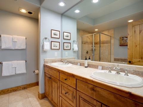 You'll love the spacious dual-sink vanity with warm wood cabinetry, soft lighting, and a glass-enclosed shower ready for your comfort and ease.