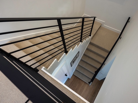 A modern staircase with sleek black railings connects the different levels of your rental, featuring neutral carpeting and contemporary design that adds architectural interest to the space.