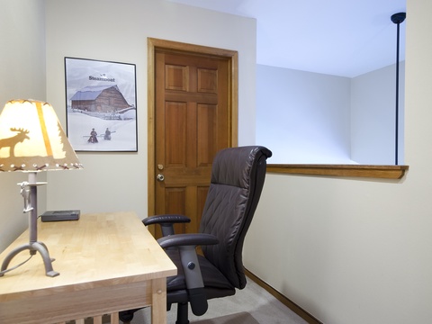 Your private workspace awaits with a rustic wooden desk, cozy moose lamp, and comfortable chair—perfect for catching up on work or planning your mountain adventures.