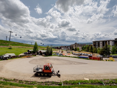 Scenic mountain resort area featuring ski lifts, green slopes, and contemporary residential buildings surrounded by natural alpine landscape under dramatic cloudy skies.