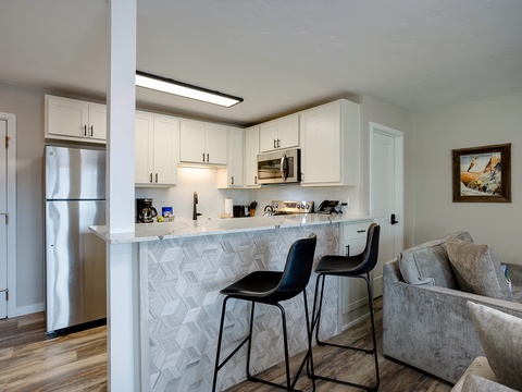 Your open-concept kitchen features white cabinetry, stainless steel appliances, and a stylish breakfast bar with marble-patterned tile backsplash—perfect for morning coffee or casual meals.