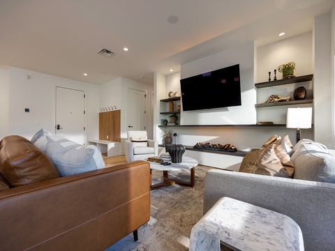 Unwind in your modern living space with plush seating, a cozy electric fireplace, and natural light flowing through the windows—perfectly styled for your comfort and relaxation.
