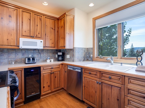Your fully-equipped kitchen invites culinary adventures with warm wood cabinetry, modern appliances, and a window framing scenic mountain views—perfect for cooking with inspiration.