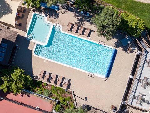 Aerial view of the property features a sparkling pool with hot tub, surrounded by lounge chairs, lush landscaping, and outdoor dining areas—a private oasis perfect for relaxation.