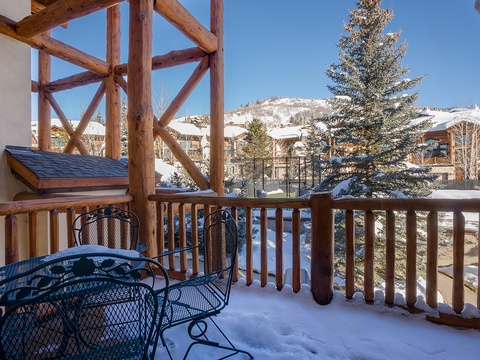Snow-dusted balcony with mountain views, evergreen trees, and a charming outdoor table—your winter retreat awaits beyond the glass doors.