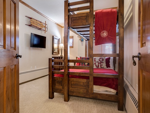 Cozy bunk room with rustic wood furnishings, a wall-mounted TV, and cheerful red bedding—perfect for family fun and mountain memories together.