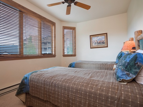 Drift into peaceful sleep in your twin bedroom with rustic touches, cooling ceiling fan, and gentle natural light filtering through wooden blinds.