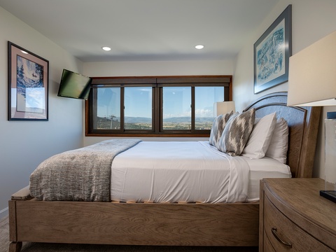 Unwind in your cozy bedroom with crisp linens and panoramic mountain views through expansive windows. Thoughtful décor and modern amenities create a peaceful retreat.