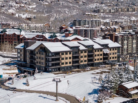 An aerial view capturing the property nestled within a snow-covered mountain resort village, with ski slopes and surrounding lodges completing the winter landscape.