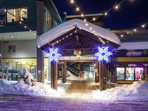 A charming winter village entrance adorned with twinkling lights and festive decorations, nestled in a snow-covered mountain setting—perfect for evening strolls and exploring nearby dining and shops.