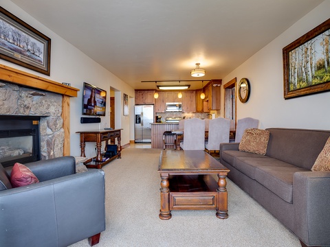 Relax in your open-plan living and dining area, complete with a cozy fireplace, modern kitchen, and comfortable seating—perfect for unwinding after a day of mountain adventures.