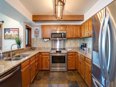 Step into your fully equipped kitchen featuring gleaming stainless steel appliances, warm wood cabinetry, granite countertops, and everything you need to prepare delicious home-cooked meals during your stay.