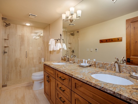 Your spacious bathroom offers dual vanities with granite counters, a walk-in shower, and warm wooden cabinetry for a luxurious retreat after a day exploring the area.