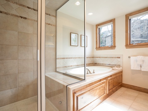 Unwind in your spacious bathroom with a deep soaking tub, walk-in shower, and natural light streaming through wood-framed windows.