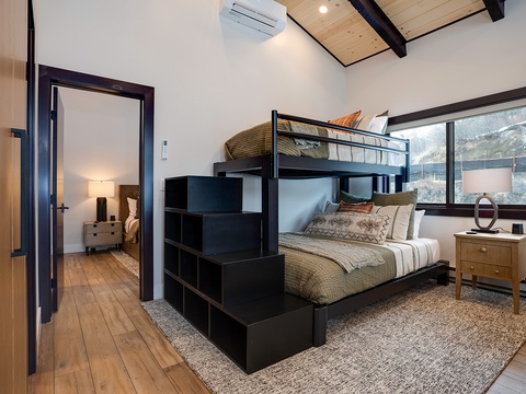 Your mountain retreat bedroom features stylish bunk beds with storage steps, letting everyone rest comfortably while enjoying natural light and scenic views through large windows.